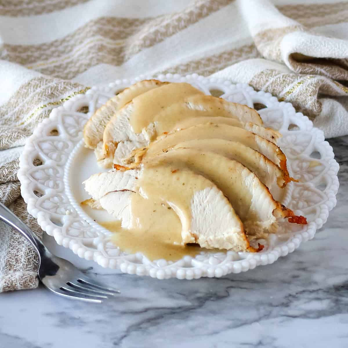 Sliced turkey with gravy spooned over the top on a white plate.