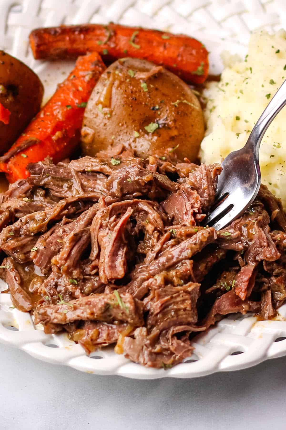 Crockpot deer roast recipe served on a white plate with carrots and potatoes.